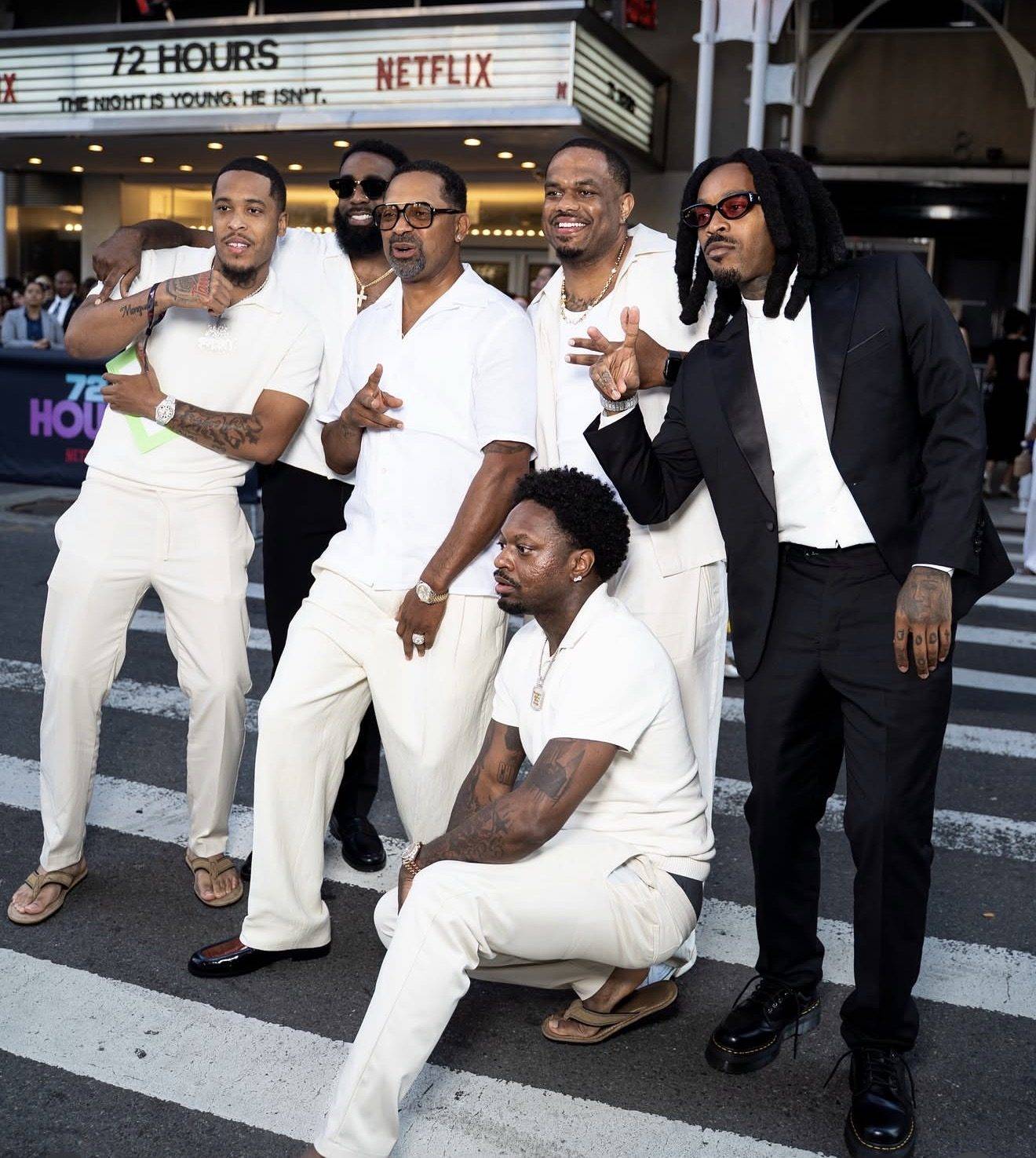 A group of six men posing on a crosswalk outside a cinema, under a marquee reading 72 HOURS and NETFLIX. Jack Funny stands at the left of the group.