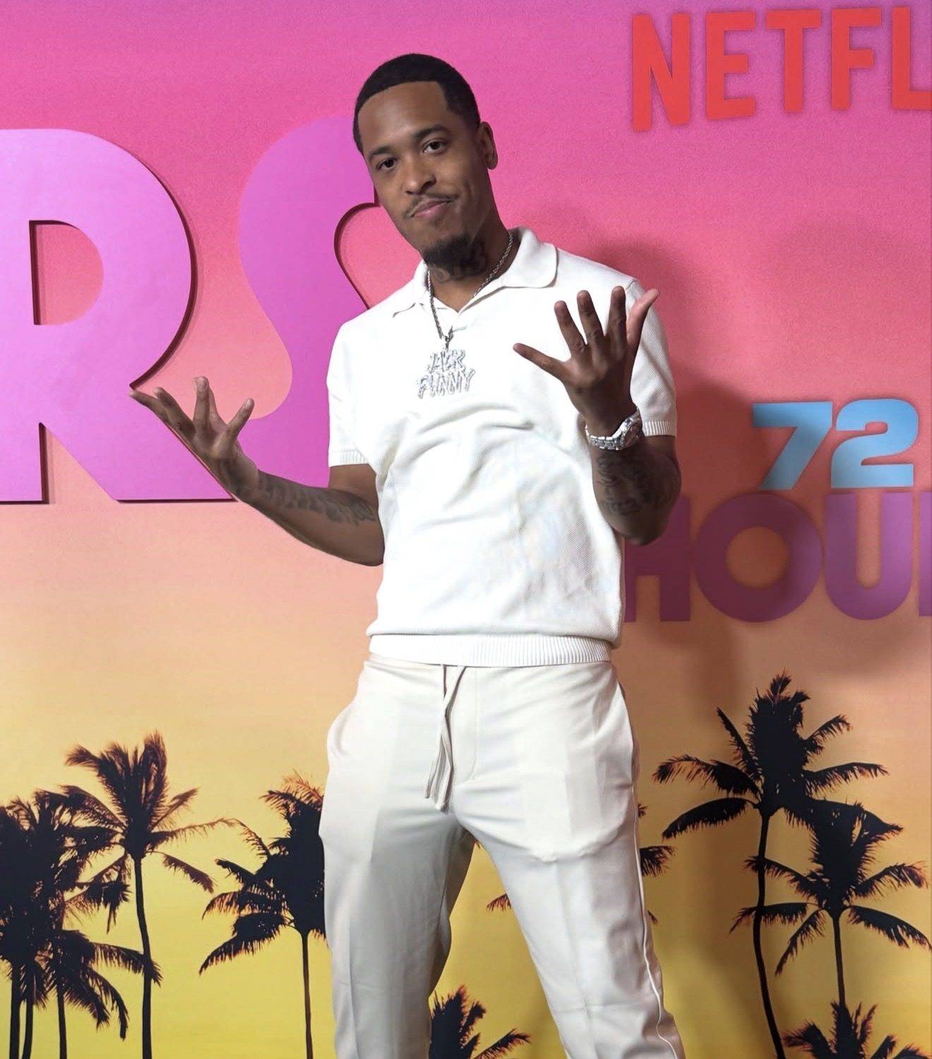 Jack Funny in an all-cream outfit and a diamond JACK FUNNY chain, arms open, standing in front of a pink-to-gold Netflix premiere step-and-repeat.